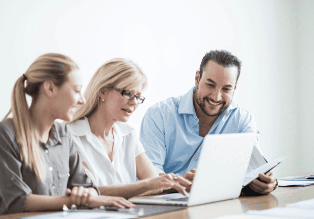 Two women and one man seated at a desk in an office and looking at a laptop Good 4 Business